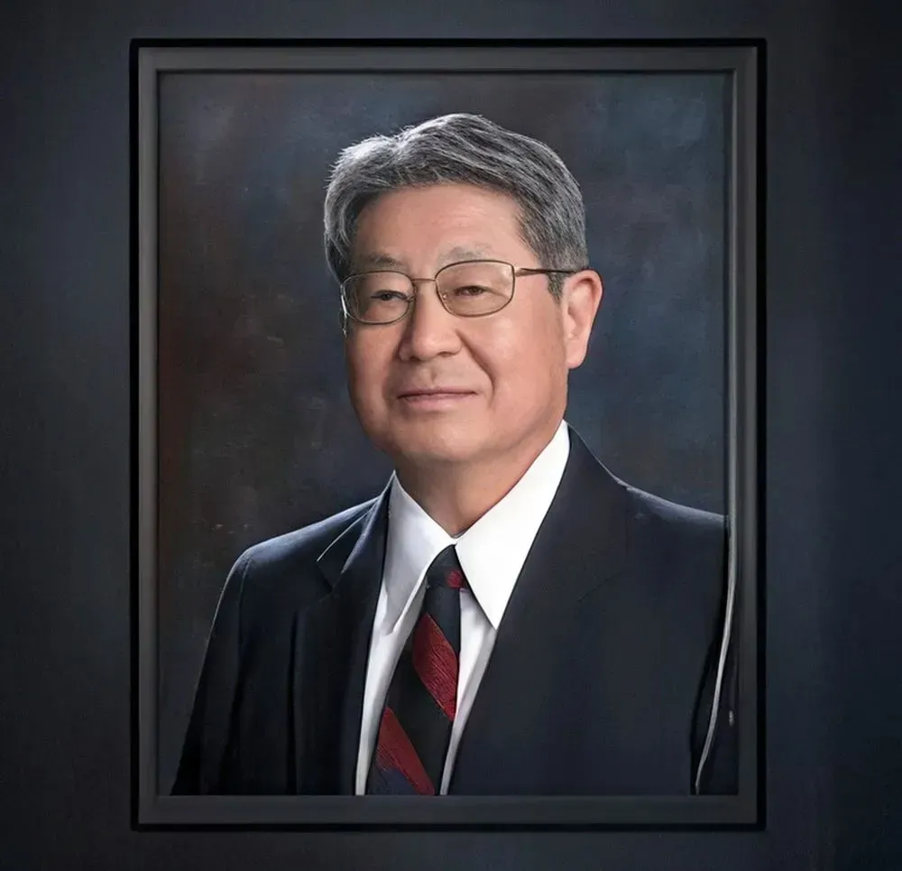 Framed formal portrait of an older man wearing glasses, suit, and striped tie.